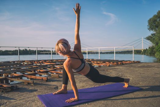 Woman practicing yoga on sunny day. Virabhadrasana, Rotated warrior pose.