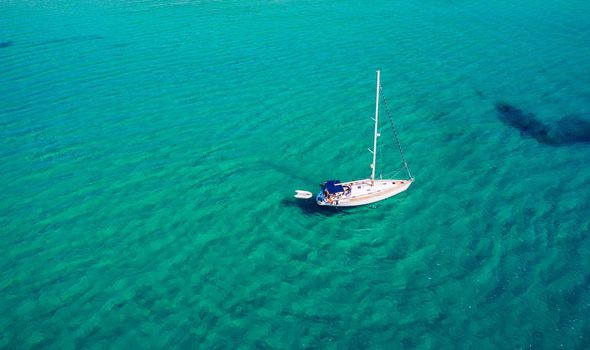 Aerial view of anchored sailing yacht in emerald sea. Aerial view of a boat. Outdoor water sports, yachting. Aerial view of anchoring yacht in open water. Ocean and sea travel and transportation