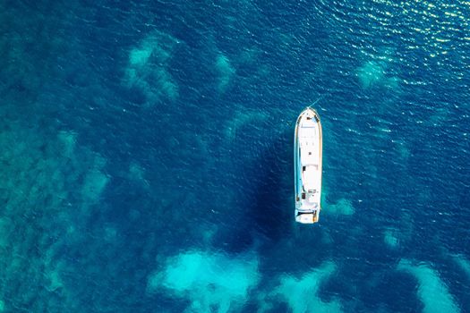 Yacht anchoring in crystal clear turquoise water in front of the tropical island, alternative lifestyle, living on a boat. Aerial view of yacht at anchor on turquoise water, showing luxury, wealth.