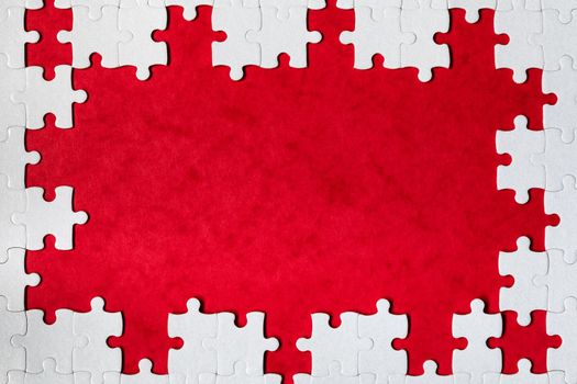 Framing in the form of a rectangle, made of a white jigsaw puzzle. Frame text and jigsaw puzzles. Frame made of jigsaw puzzle pieces on red background.