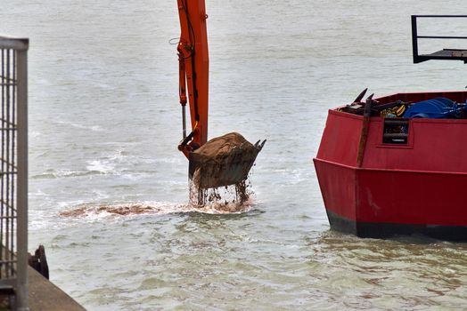 A close up of the bucket of digger full of sand and mud from the ocean floor