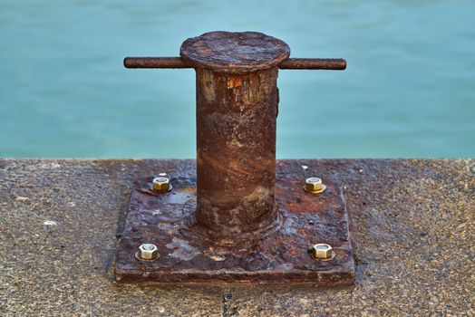 The heavy steel pillar bollard is mounted on a harbour wall for securing boats while docking in port.