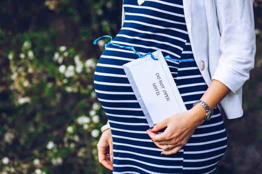 Closeup of a pregnant belly with a blue ribbon and a tag saying do not open until...Pregnant belly with a light blue ribbon and a tag saying do not. Mother, expecting.