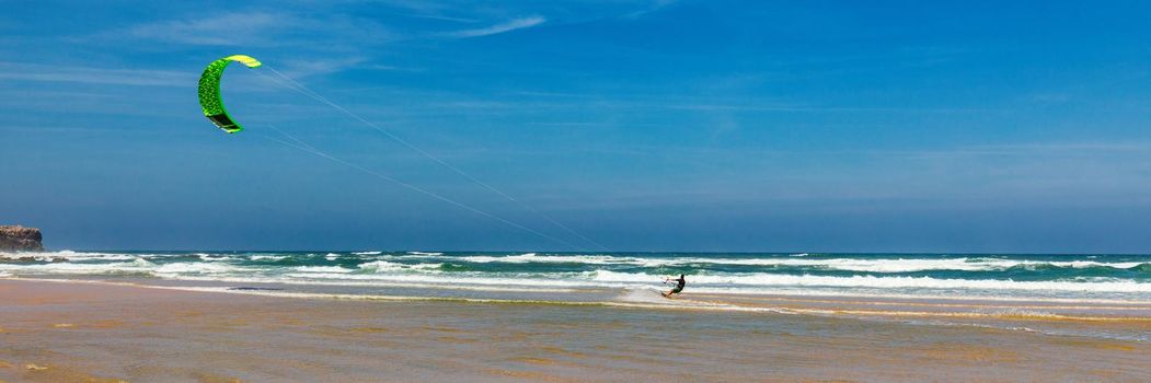 Surfers in Praia da Bordeira beach near Carrapateira, Portugal. Kiteboarder kitesurfer athlete performing kitesurfing kiteboarding tricks. Praia da Bordeira is popular location for surfing. Portugal