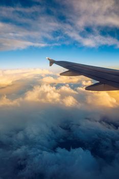 Flying and traveling, view from airplane window on the wing on sunset time. Aircraft wing under the earth and clouds. Flight in sky. Looking over aircraft wing in flight. 
