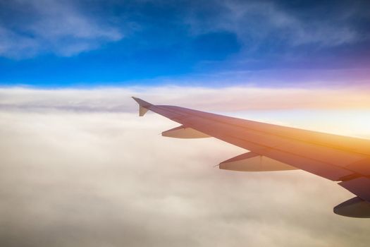 Flying and traveling, view from airplane window on the wing on sunset time. Aircraft wing under the earth and clouds. Flight in sky. Looking over aircraft wing in flight. 
