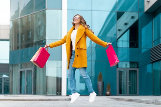Business Woman With Shopping Bags Dressed Yellow Coat Jumping With Happiness Outdoors Corporative Building Caucasian Female Business Person Near Office Building Stylish Businesswoman Season Sale