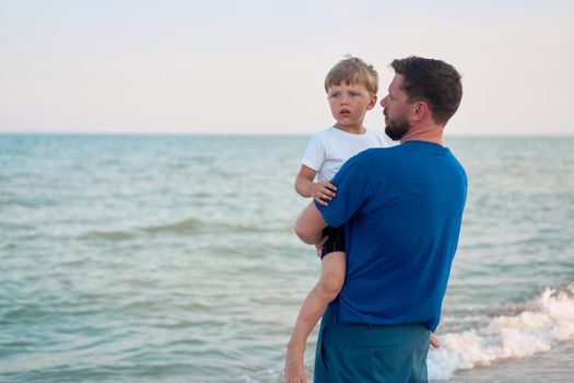 Father son spending time together sea vacation Young dad child little boy walking beach Fathers day. Family with one child. Happy childhood with daddy. sitting on hands laughs