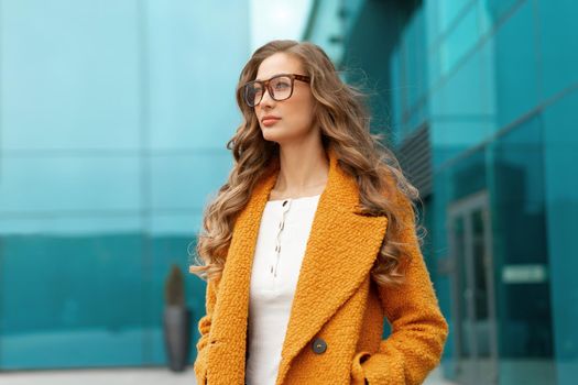 Business woman dressed yellow coat standing outdoors corporative building background Caucasian female business person eyeglasses on city street near office building big windows Stylish businesswoman