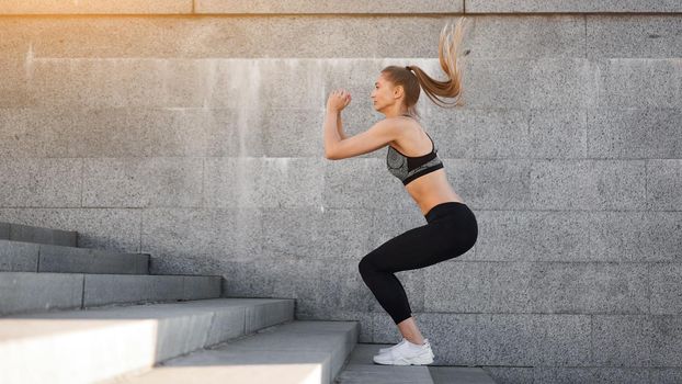 Urban sporty woman training. Female athlete doing squat jumps on urban stairs. Fitness motivation Healthy lifestyle concept