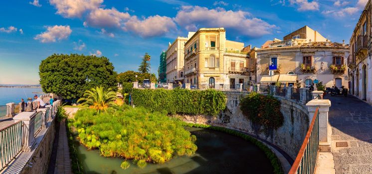 The Fountain of Arethusa and Siracusa (Syracuse) in a sunny summer day. Sicily, Italy. The Fountain of Arethusa in Ortygia, historical centre of Syracuse, Sicily, Italy.