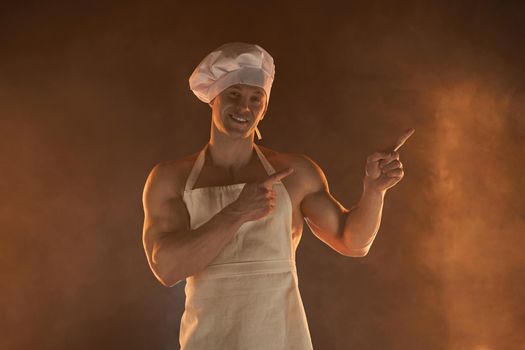 New normal concept. Portrait of muscular chef wearing protective medical mask white apron and cheef hat, standing on smoky background and lamp light male housewife. husband in kitchen. brutal butcher.