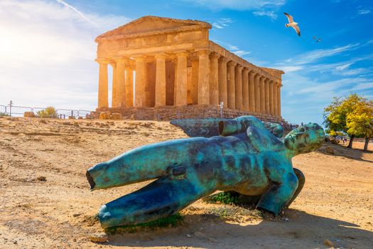 Bronze statue of Icarus in front of the Temple of Concordia at the Valley of the Temples. Temple of Concordia and the statue of Fallen Icarus, in the Valley of the Temples, Agrigento, Sicily, Italy.