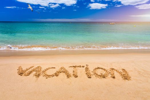Vacation text on a beach. Vacation written in a sandy tropical beach. "Vacation" written in the sand on the beach blue waves in the background. Vacation on the sand beach concept.
