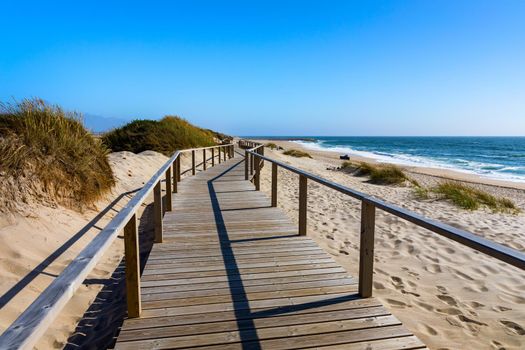 Wooden path at Costa Nova d'Aveiro, Portugal, over sand dunes with ocean view, summer evening. Wooden footbridge of Costa Nova beach in a sunny day. Aveiro, Portugal. 
