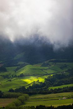 Bright sunlight shining through hole of clouds to dark scene of mountain range, Azores, Sao Miguel, Portugal. The beam of light through the dark clouds on the mountains in Azores, Portugal.