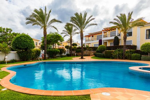Great backyard with swimming pool, hot tub and lounge chairs. Swimming pool in backyard. Incredible swimming pool and garden with palm trees and flowers in a sunny day.