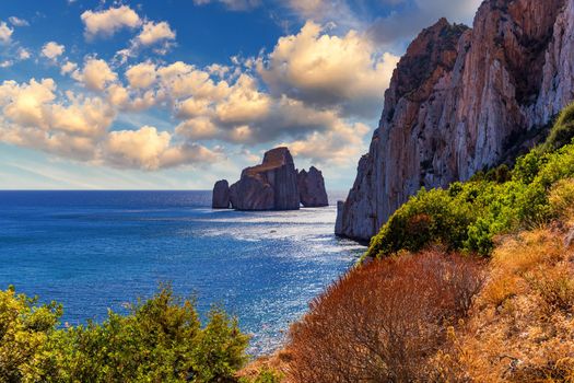 High cliffs of Mediterranean coast, "Pan di Zucchero" stack rock in Masua, west coast of Sardinia, Italy. Concali Su Terrainu with Porto Corallo on background. Sardinia island, Italy, Europe.