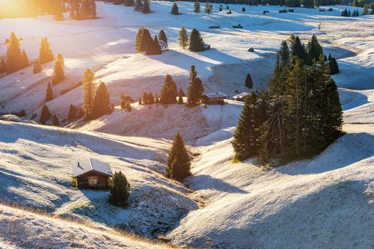 Small wooden farm house, cottage or log cabins on meadow on Alpe di Siusi, Seiser Alm. Alpe di Siusi or Seiser Alm with Sassolungo, Langkofel mountain group, Dolomite Alps, South Tyrol, Italy.