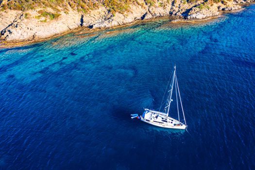 Yacht anchoring in crystal clear turquoise water in front of the tropical island, alternative lifestyle, living on a boat. Aerial view of yacht at anchor on turquoise water, showing luxury, wealth.