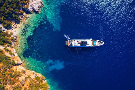 Yacht anchoring in crystal clear turquoise water in front of the tropical island, alternative lifestyle, living on a boat. Aerial view of yacht at anchor on turquoise water, showing luxury, wealth.