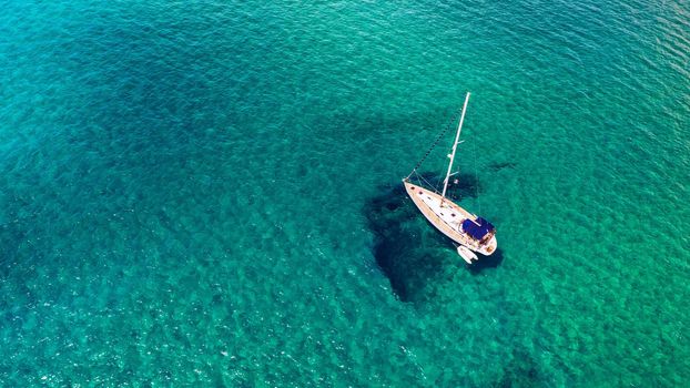 Yacht anchoring in crystal clear turquoise water in front of the tropical island, alternative lifestyle, living on a boat. Aerial view of yacht at anchor on turquoise water, showing luxury, wealth.