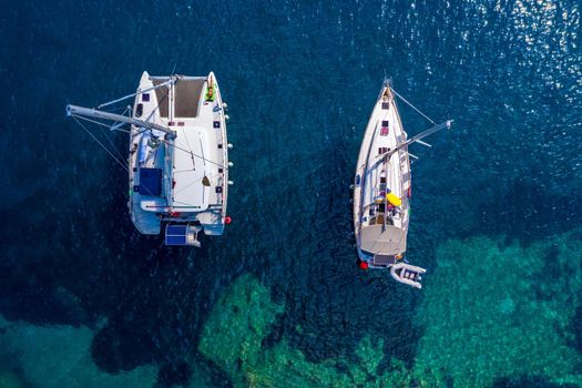 Aerial view of anchored sailing yacht in emerald sea. Aerial view of a boat. Outdoor water sports, yachting. Aerial view of anchoring yacht in open water. Ocean and sea travel and transportation