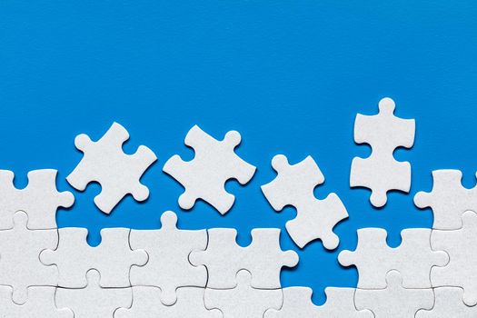 White jigsaw puzzle. White puzzle pieces on color background. Unfinished white jigsaw puzzle pieces on color background. 