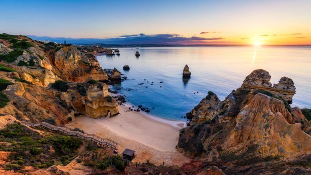Sunrise at Camilo beach in Lagos, Algarve, Portugal. Wooden footbridge to the beach Praia do Camilo, Portugal. Picturesque view of Praia do Camilo beach in Lagos, Algarve region, Portugal.