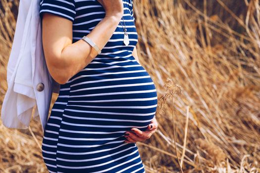 Beautiful pregnant woman feeling happy in nature while taking care of her child. Young expecting mother holding baby in pregnant belly. Maternity prenatal care and woman pregnancy concept.