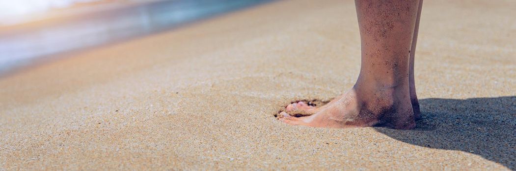 Closeup on leg of young woman standing on sea shore. Woman legs and feet walking on the sand of the beach with the sea water in the background. Woman standing on the beach with wave sea.
