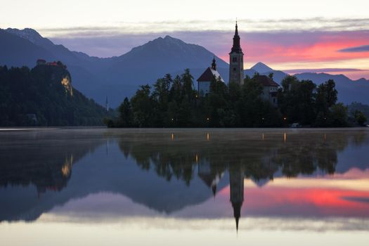 Dramatic sunrise on lake Bled, sunrise view on Bled lake, island, Pilgrimage Church of the Assumption of Maria and Castle with mountain range (Stol, Vrtaca, Begunjscica). Bled, Slovenia,