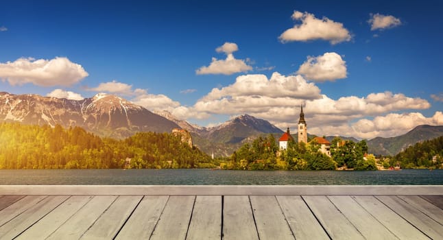 Empty wooden table in front of abstract blurred background in nature, can be used for display or montage your products. Mock up for display of product. Bled island in the background from Slovenia.