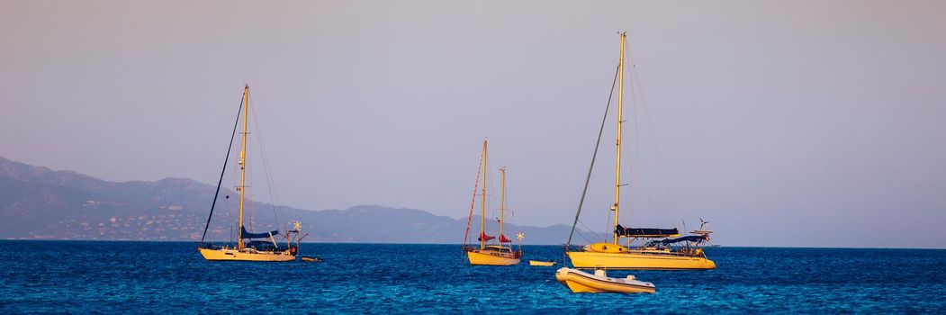 Yacht anchoring in crystal clear turquoise water in front of the tropical island, alternative lifestyle, living on a boat. Aerial view of yacht at anchor on turquoise water, showing luxury, wealth.