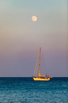 Aerial view of anchored sailing yacht in emerald sea. Aerial view of a boat. Outdoor water sports, yachting. Aerial view of anchoring yacht in open water. Ocean and sea travel and transportation