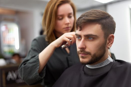 Stylish man sitting barber shop Hairstylist Hairdresser Woman cutting his hair Portrait handsome happy young bearded caucasian guy getting trendy haircut Attractive barber girl working serving client