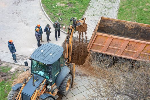 BELARUS, MINSK - MAY 17, 2021: A tractor with an excavator bucket digs a hole and loads sand into the back of a dump truck. Stock photography.