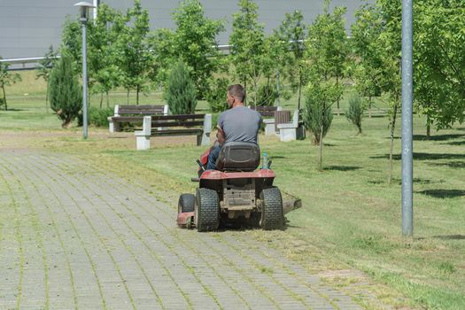A man drives a lawn mower and drives along the sidewalk, Blurred background. Stock photography.