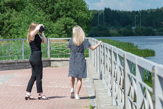 Girl photographer photographs a model near the fence on the embankment, blurred background. Stock photography.