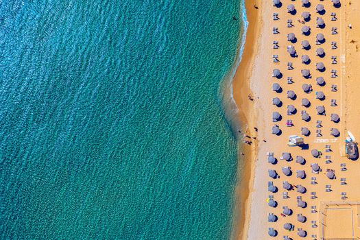 View from above, stunning aerial view of an amazing beach with beach umbrellas and turquoise clear water. Top view on sun loungers under umbrellas on the sandy beach. Concept of summer vacation. 