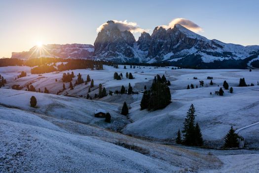 Small wooden farm house, cottage or log cabins on meadow on Alpe di Siusi, Seiser Alm. Alpe di Siusi or Seiser Alm with Sassolungo, Langkofel mountain group, Dolomite Alps, South Tyrol, Italy.