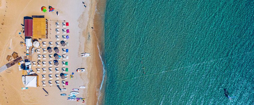 View from above, stunning aerial view of an amazing beach with beach umbrellas and turquoise clear water. Top view on sun loungers under umbrellas on the sandy beach. Concept of summer vacation. 