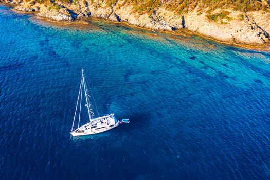 Aerial view of anchored sailing yacht in emerald sea. Aerial view of a boat. Outdoor water sports, yachting. Aerial view of anchoring yacht in open water. Ocean and sea travel and transportation