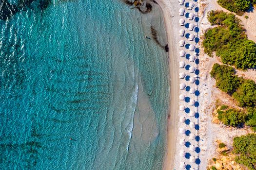 View from above, stunning aerial view of an amazing beach with beach umbrellas and turquoise clear water. Top view on sun loungers under umbrellas on the sandy beach. Concept of summer vacation. 