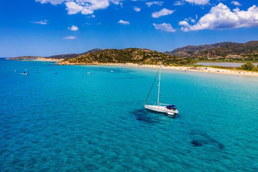 Yacht anchoring in crystal clear turquoise water in front of the tropical island, alternative lifestyle, living on a boat. Aerial view of yacht at anchor on turquoise water, showing luxury, wealth.
