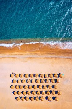View from above, stunning aerial view of an amazing beach with beach umbrellas and turquoise clear water. Top view on sun loungers under umbrellas on the sandy beach. Concept of summer vacation. 