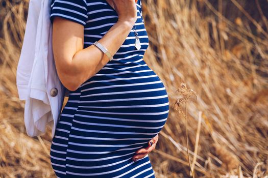 Beautiful pregnant woman feeling happy in nature while taking care of her child. Young expecting mother holding baby in pregnant belly. Maternity prenatal care and woman pregnancy concept.