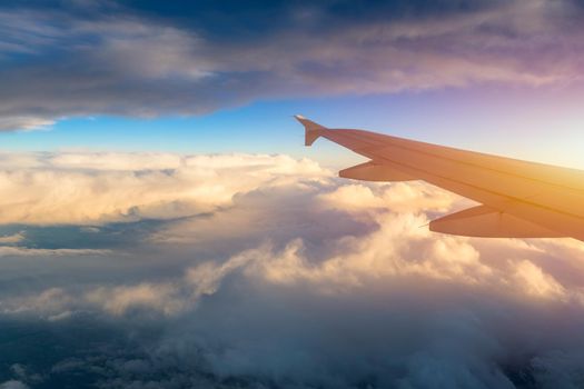 Flying and traveling, view from airplane window on the wing on sunset time. Aircraft wing under the earth and clouds. Flight in sky. Looking over aircraft wing in flight. 
