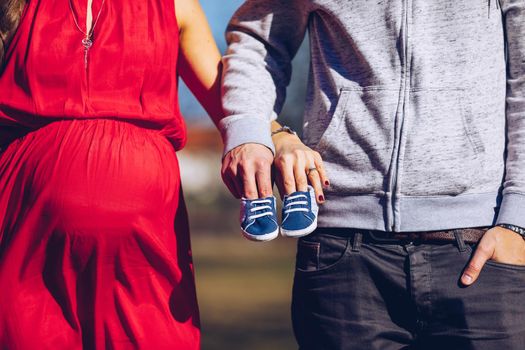 Young couple waiting for baby. Expecting parents with little baby boy shoes. Concept of Parents-To-Be. Shoes and sneakers of parents and expected baby. Mom, dad and the future baby Shoes.