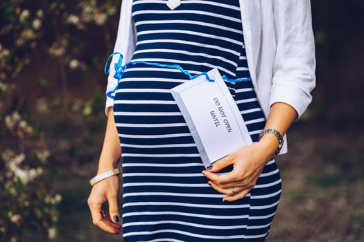 Closeup of a pregnant belly with a blue ribbon and a tag saying do not open until...Pregnant belly with a light blue ribbon and a tag saying do not. Mother, expecting.